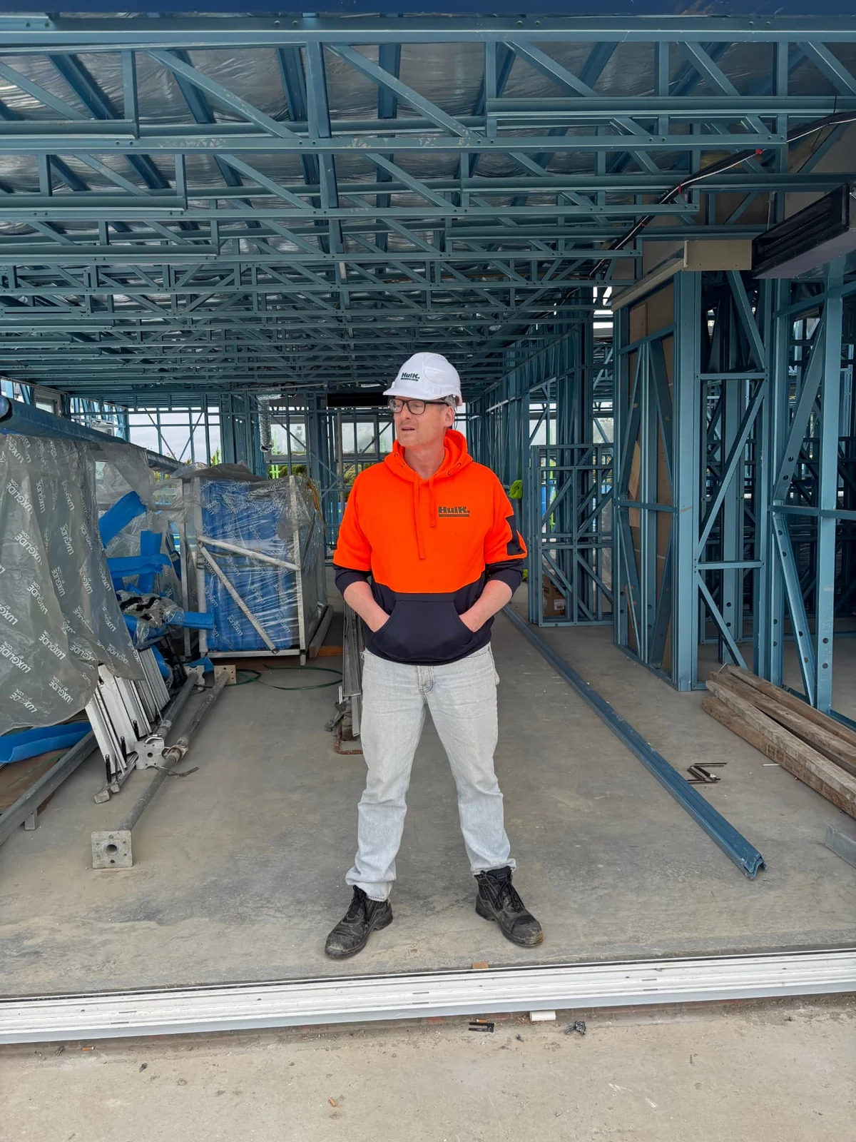 Hulk worker in a white hard hat and orange high-visibility clothing on a framed construction site
