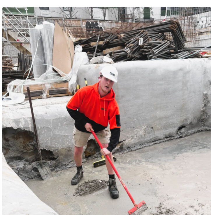 Hulk worker in a hard hat and branded hoodie finishing a concrete slab on site
