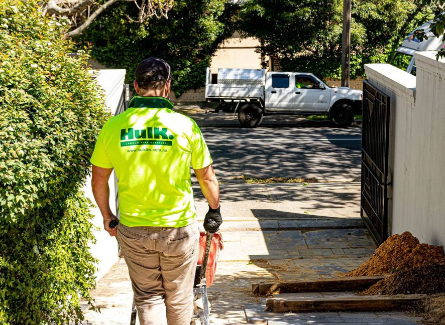 Hulk worker in a branded high-visibility shirt walking down a driveway towards a residential job site