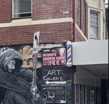 Street view of Melbourne artwork beside Oliver's Barber Shop and the Art Gallery on a red-brick corner building