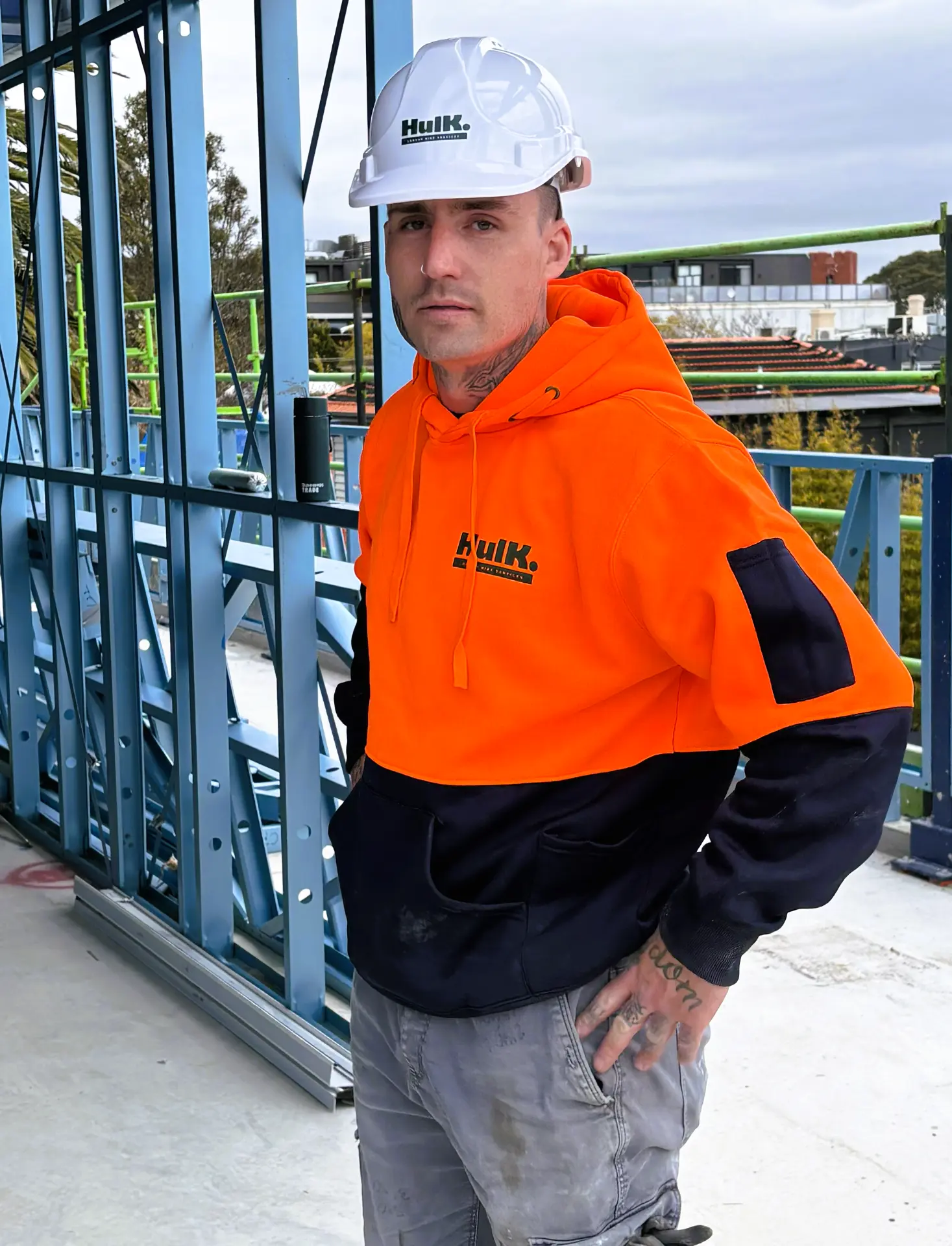 Hulk worker in a white branded hard hat and orange high-visibility Hulk hoodie on a steel-frame construction site