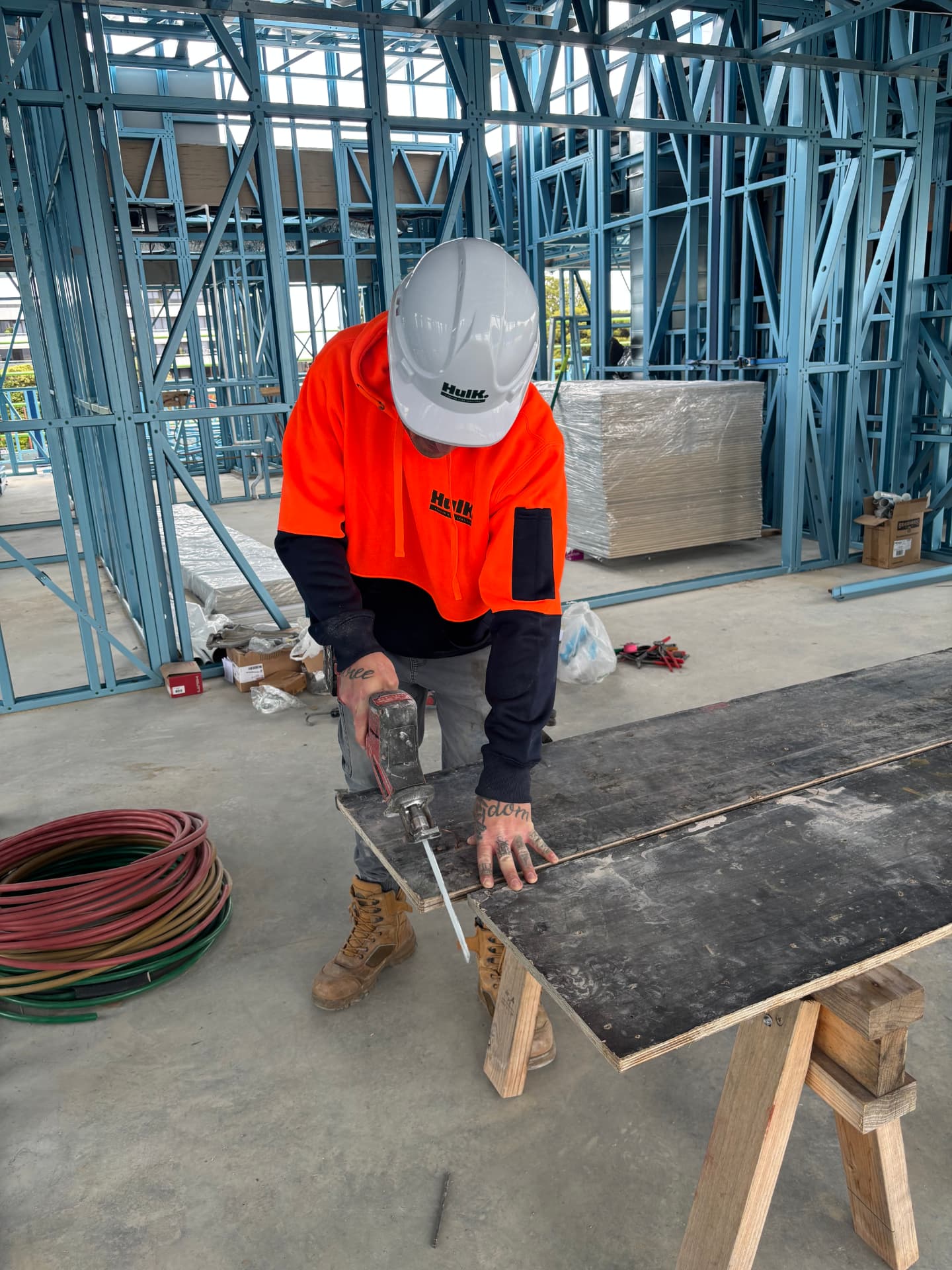 Hulk trade assistant in a hard hat and branded hoodie cutting board on site